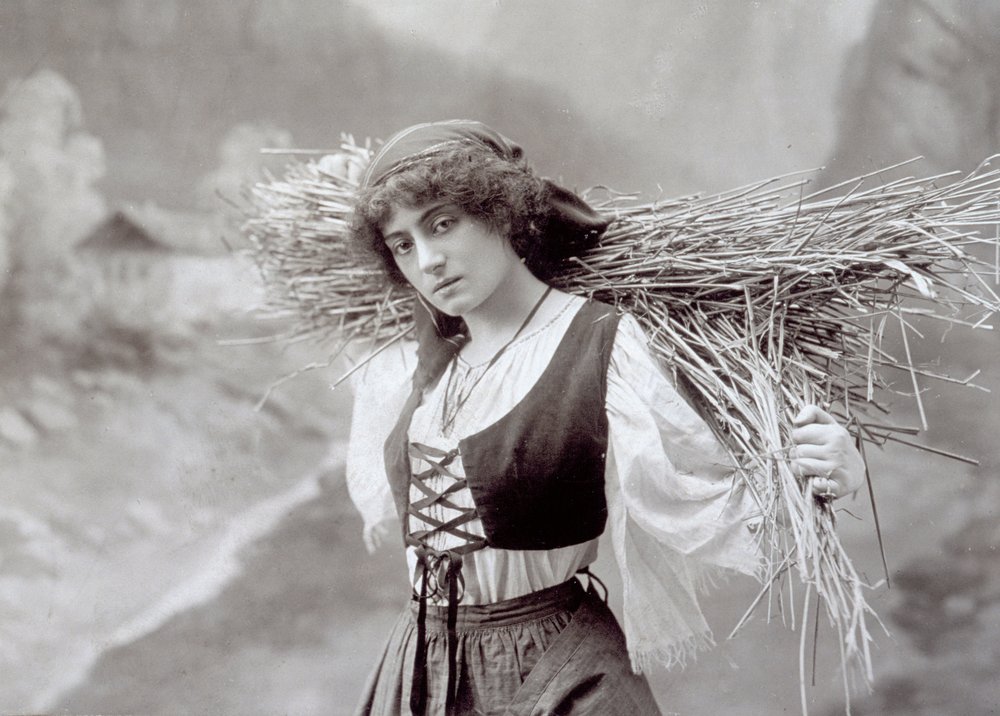 藁の束を運ぶ民族衣装の若い女性（モノクロ写真