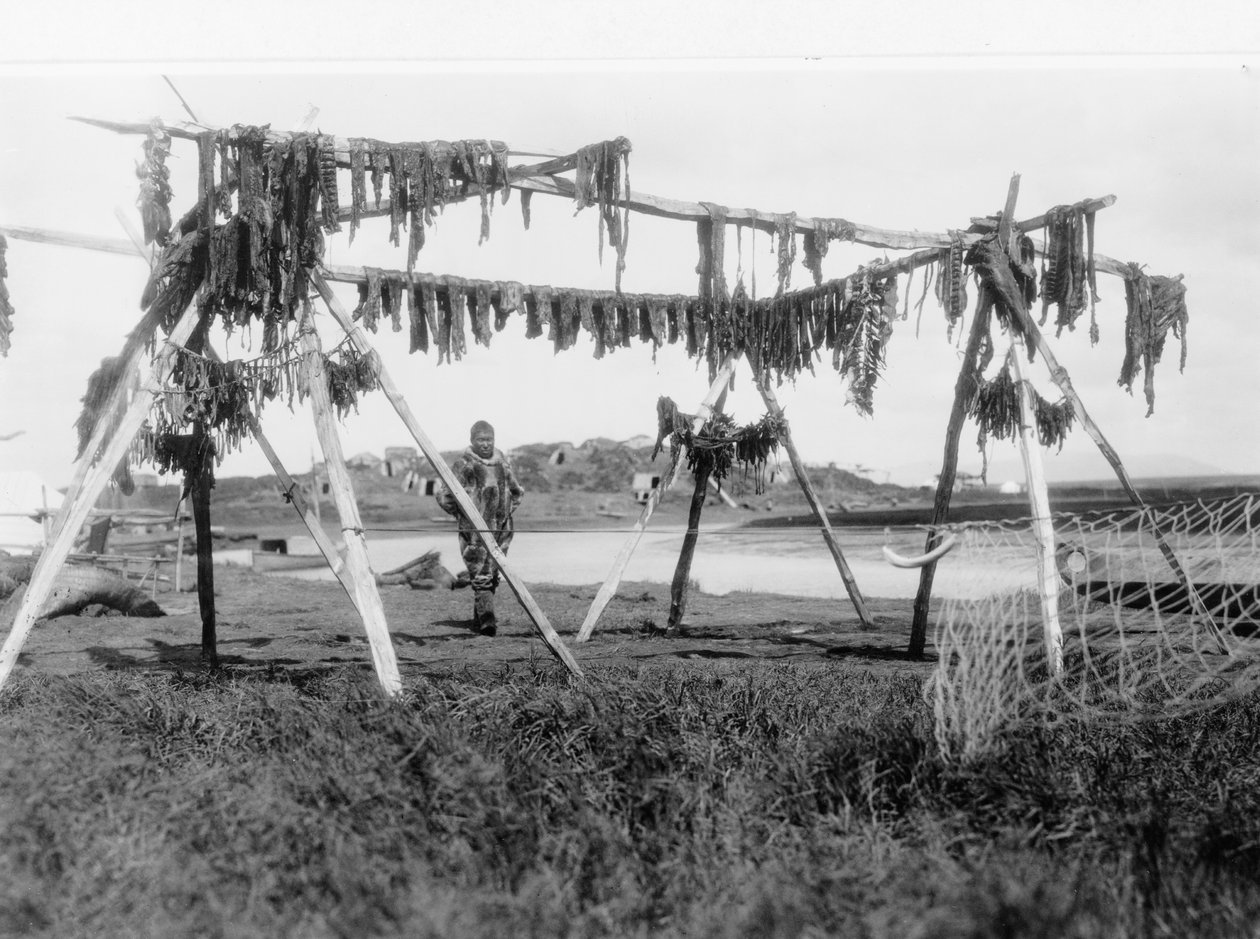 クジラの肉が吊るされた構造物の下に立つエスキモーの男性、1929年頃（白黒写真） 作： エドワード保安官カーティス