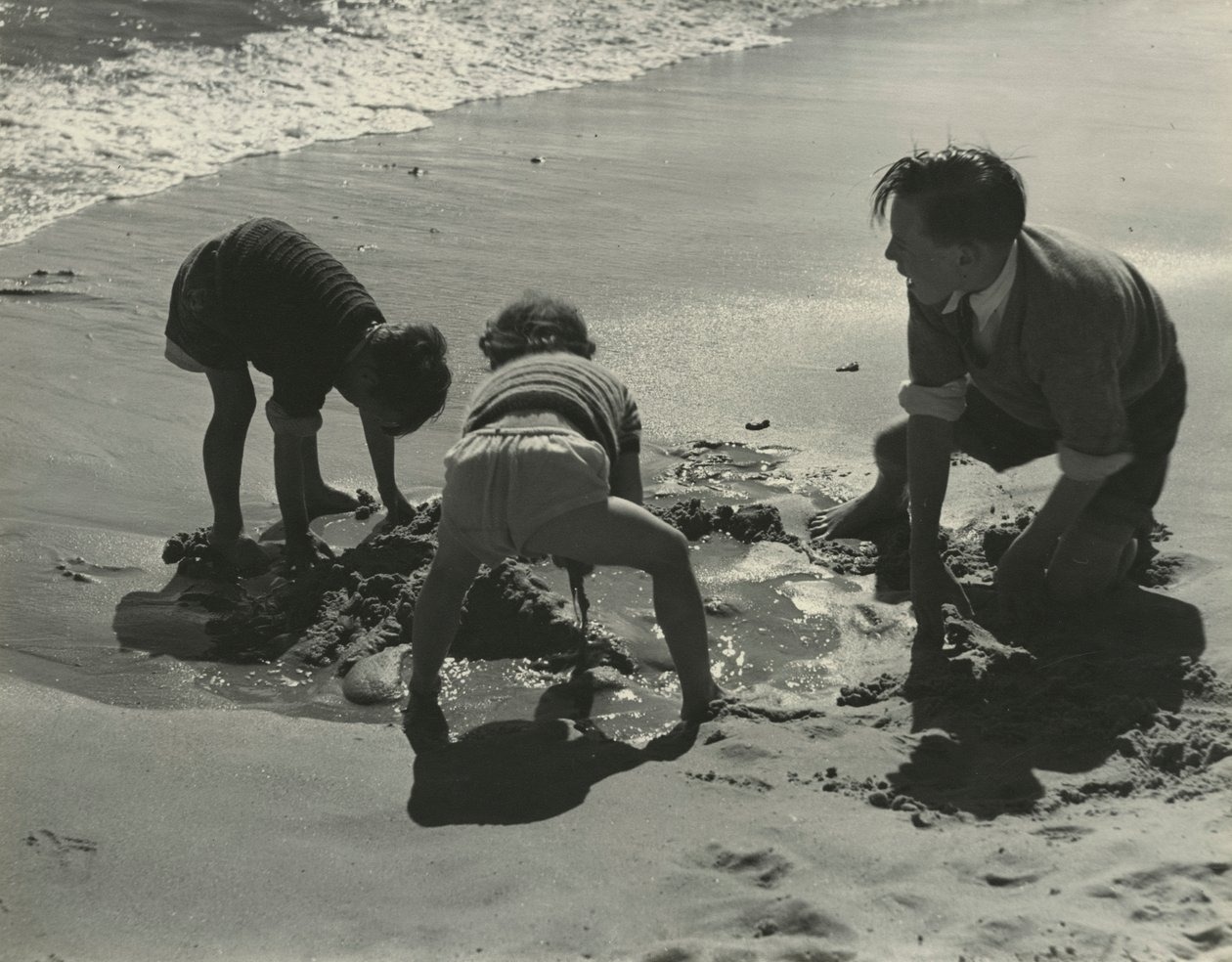 ビーチで砂遊びをする3人の子供たち。 作： ゴッドフリー・マクドミニク
