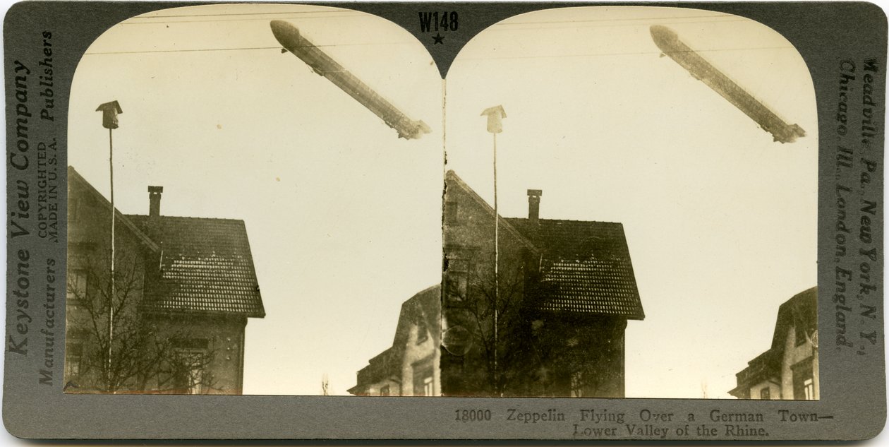 ツェッペリン型飛行船が町の屋根の上を飛んでいる、セピア色の横型ステレオカード。 Keystone Stereograph number18000。タイトルは 作： Keystone View Company