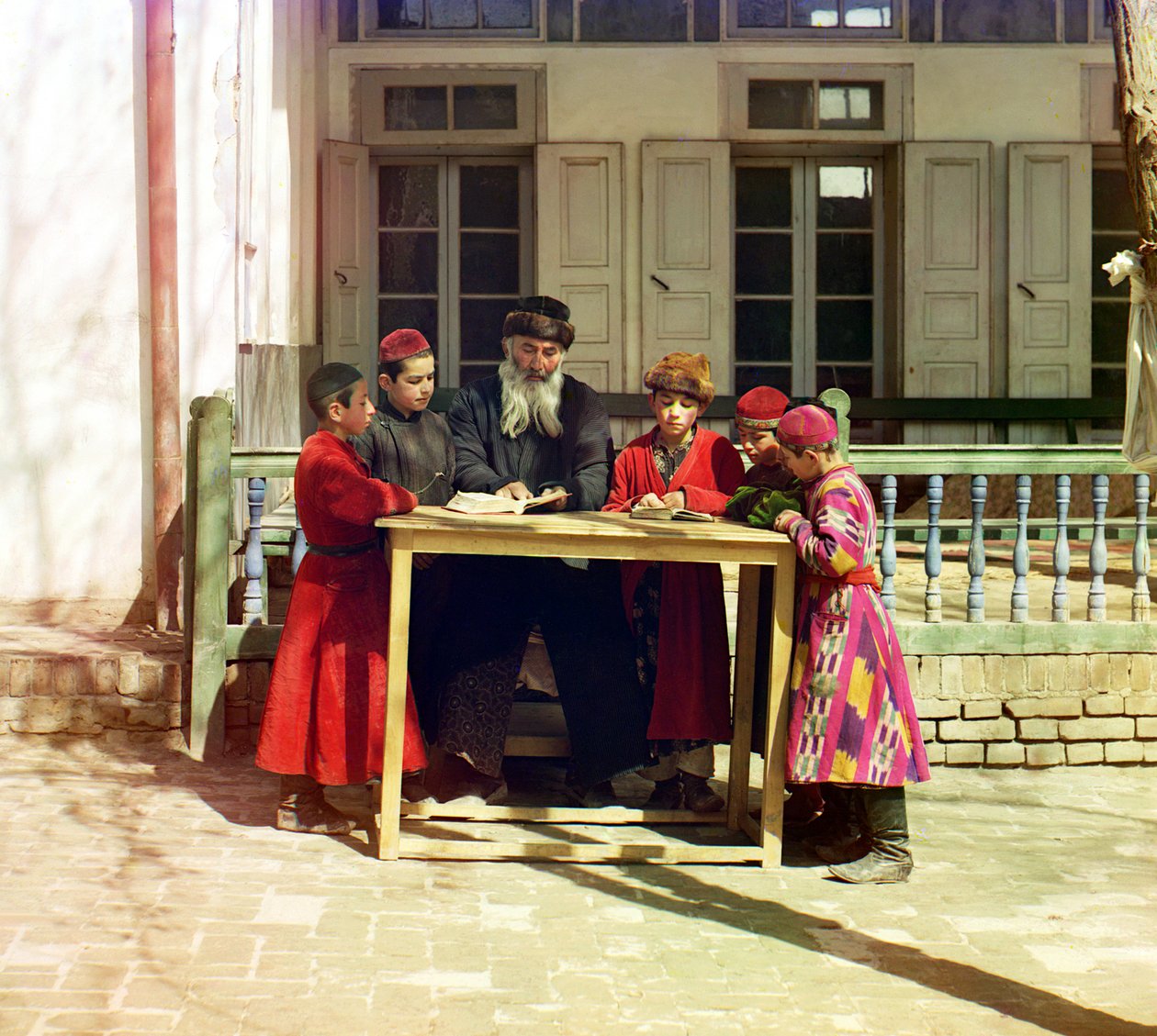 1905年から1915年の間にロシア帝国サマルカンドの家の前のテーブルに教師がいるユダヤ人の子供たちのグループ 作： セルゲイ・プロクディン・ゴルスキー