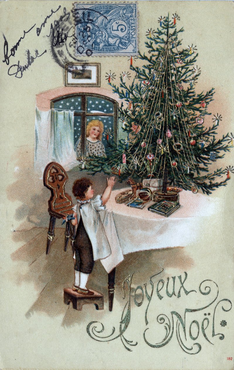 クリスマス・グリーティングカード：テーブルの上に置かれたクリスマスツリーの前でポーズをとる子供と、窓から見える天使 - 1905年のポストカード 作： 不明