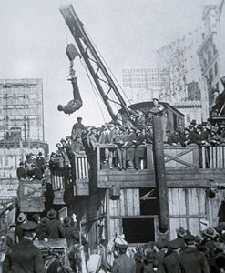 ニューヨークのクレーンに吊られて拘束衣を脱ぐフーディーニ（モノクロ写真 作： American Photographer