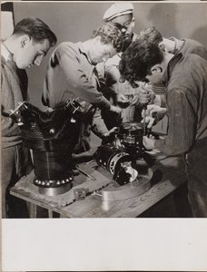 [5人の若者が作業台の周りで働いている] 作： Arnold Eagle