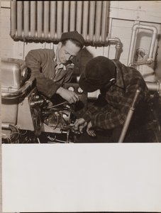[2人の男がドライバーとレンチを使って機械を操作する] 作： Arnold Eagle