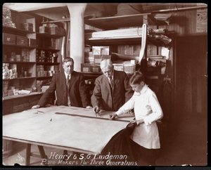 ヘンリーとSGリンデマンの肖像画。息子または孫がピアノの店の図面の上に立っています。1910年（銀ゼラチンプリント）