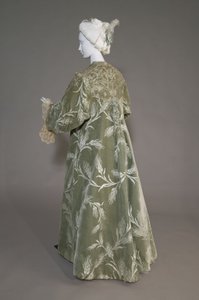 バーサ・パーマーのイブニング・コート、1902年頃（背面斜視図）。シルクサテンに小麦柄のカットベルベット、金属糸のレース、シルクのメタリックタッセル。パリのワース社。