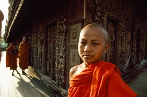 チーク材の彫刻パネルの前にいる若い修行僧。ビルマ、マンダレー、シュエナンドー僧院。