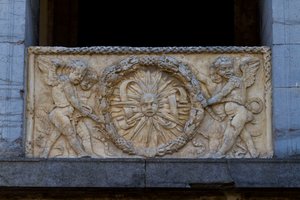 サン・セバスティアーノ教会のファサードの浅浮彫りになった花輪の中の光線状の太陽が描かれた欄干プレート