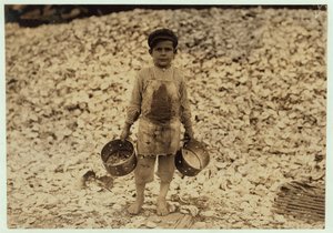 1911年、ミシシッピ州ビロクシにあるダンバー、ロペス、デュケイトカンパニーで2年目を過ごした、カキの殻の山の前で働く5歳の移民エビピッカーマヌエル 作： Lewis Wickes Hine
