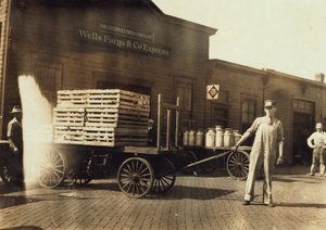 1916年、ミズーリ州スプリングフィールドにあるクレートとミルク缶を備えたウェルズファーゴウントコエクスプレスデポの前に立つ男性 作： Lewis Wickes Hine