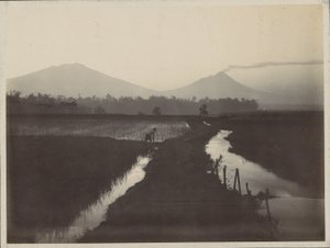 噴火する火山のふもとで土地を耕す男