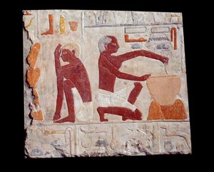 古代エジプトのアート：パンを焼く。一人がケーキのペーストを作り、もう一人がパンの型の焼き上がりを監視している。石灰岩（紀元前2500-2350年）第5王朝時代。パリ、ルーヴル美術館（Musee Du Louvre