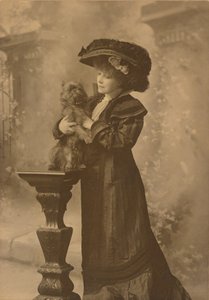 [スタジオに立つサラ・ベルナールは、木彫りの豪華な台座の上に小さな黒い犬を抱いている] 作： Theodore C. Marceau