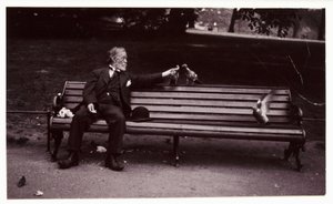 Man on a park bench, c 1920 公園のベンチに座ってハトに餌をやっている男性のスナップショット写真。 作： Unbekannt