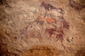 ロックアート、先史時代。スーダンのウワイナット山塊に描かれた、装飾されたシェルターの中にいる牛の群れと多色のキャラクター（羊飼いと弓矢）の岩絵。紀元前8000年から3000年の時代。写真撮影 作： Unbekannt