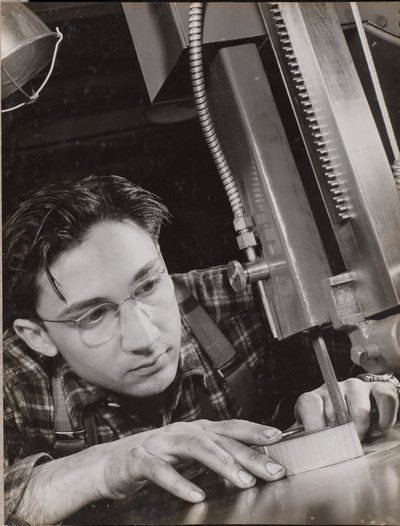 [眼鏡をかけた男が工業用ヤスリで熱心に作業している] 作： Arnold Eagle