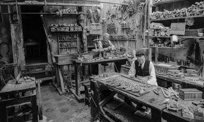 工房の作業台で木製の小物を製作する職人たち。 作： Bernard F. Rogers