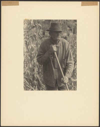 [ソルガム畑で鍬を持つ男] 作： Doris Ulmann