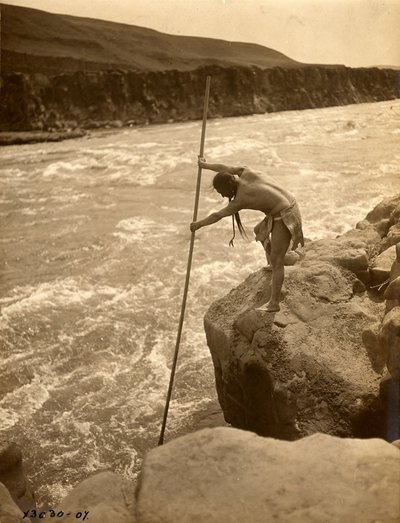 岩の上に立ち、つけ網で漁をするトラクルイト・インディアン、1910年頃（モノクロ写真） 作： エドワード保安官カーティス