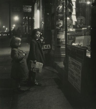 冬のコートを着た2人の少女が夜の店の外に立っている。 作： Godfrey Macdominic