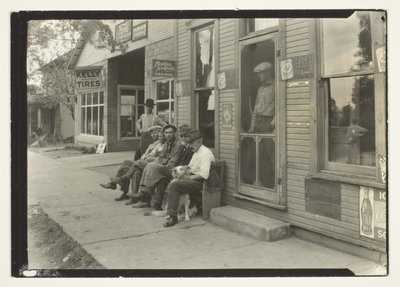 雑貨店の前のベンチに座る犬を連れた男たち 作： Lewis Wickes Hine