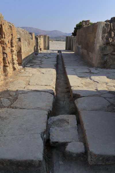 ミノア時代のファイストスの考古学的遺跡。北翼の門の後ろにある排水管付きの広い回廊は、中央の中庭から開かれ、王の居室の隣にある中庭につながっている。クレタ島のファイストス。 作： Minoan