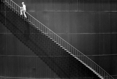 石油貯蔵タンク脇の階段を登る男。 作： Ted Spiegel