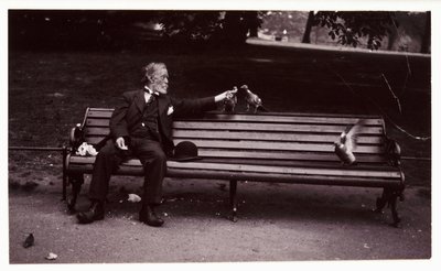 Man on a park bench, c 1920 公園のベンチに座ってハトに餌をやっている男性のスナップショット写真。 作： Unbekannt