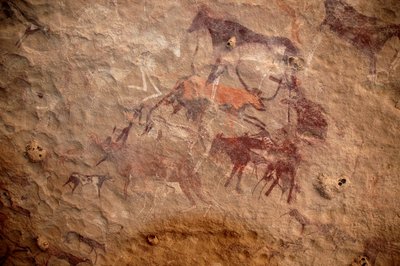 ロックアート、先史時代。スーダンのウワイナット山塊に描かれた、装飾されたシェルターの中にいる牛の群れと多色のキャラクター（羊飼いと弓矢）の岩絵。紀元前8000年から3000年の時代。写真撮影 作： Unbekannt