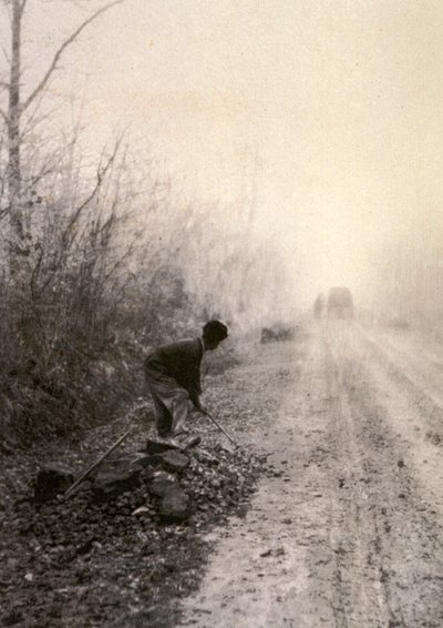 朝もやに包まれた田舎道。手前では男が石を割っている。 作： Unbekannter Künstler
