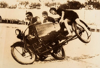 若い女性3人を乗せたサイドカー付きオートバイの運転を披露する男。曲がるとサイドカーが地面から浮き上がる。 作： Unknown photographer