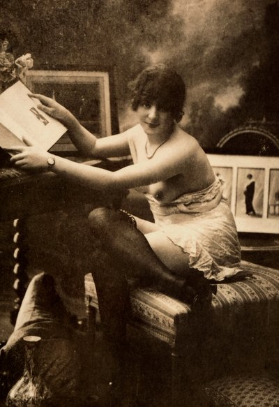 テーブルに座って本を読む、親しげな服装の若い女性の肖像。 作： Unknown photographer