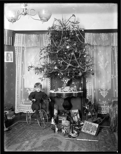 シーモア少年は、パーラーでクリスマスツリーの横にある三輪車に座ってポーズをとった、1912年のクリスマス 作： William Davis Hassler