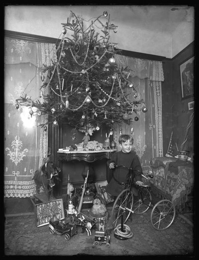パーラーのクリスマスツリーの横にある三輪車でポーズをとったセイモア少年、クリスマス1912 作： William Davis Hassler