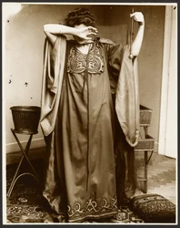 [片手を顔に当て、もう片方の手にオーブを持って立つ女性モデル]。