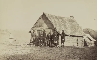 兵士のグループと1人のアフリカ系アメリカ人である2人の若い男性は、1861年から65年の丸太小屋の外に立っています。