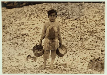 1911年、ミシシッピ州ビロクシにあるダンバー、ロペス、デュケイトカンパニーで2年目を過ごした、カキの殻の山の前で働く5歳の移民エビピッカーマヌエル