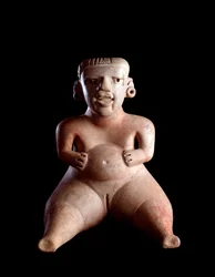 マヤ文明・先史時代：グアテマラ・カミナルジュユ出土の、腹を膨らませて足を開いた座位の女性を描いた粘土像（産婦？寸法19 x25 cm グァテマラ国立考古学・民族学博物館 先 コロンビア