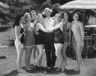 Hollywood, California: c.1935 水着を着た7人の若い女性が一人の男性の注目を集めようと争っている。(白黒写真)