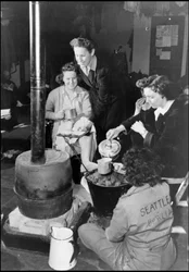 第二次世界大戦（1939-1945）：WAC（女性陸軍部隊）の部隊が収容されているイギリスの空軍基地で、シャンブルのストーブを囲んでおやつをとる一団。写真は1943年。