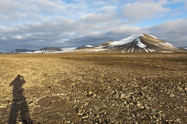 人の影、プラタベルゲ山の多角形構造土、背景に雪を頂くノルデンショルドフィエレ山、ロングイェールビーン近郊、スピッツベルゲン島、スヴァールバル諸島、ノルウェー、ヨーロッパ