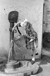 ポンプの噴水でバケツの水を空にする少女、1939年5月9日（モノクロ写真）