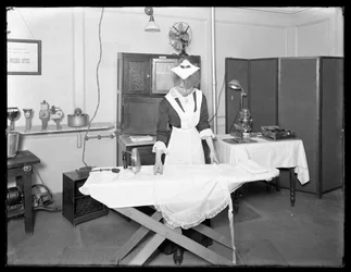 電気アイロンの使用を示すメイドの衣装を着た若い女性、c.1913-14